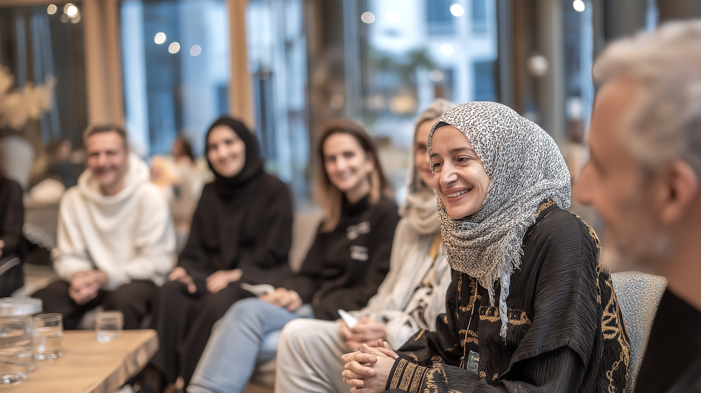 6 unterschiedliche Personen sitzen zusammen an einem Tisch und hören lächelnd zu